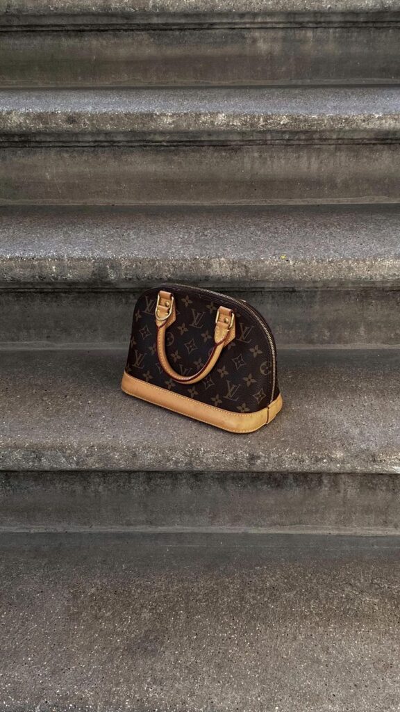 Structured Louis Vuitton Alma handbag in monogram canvas on a minimalist marble background
